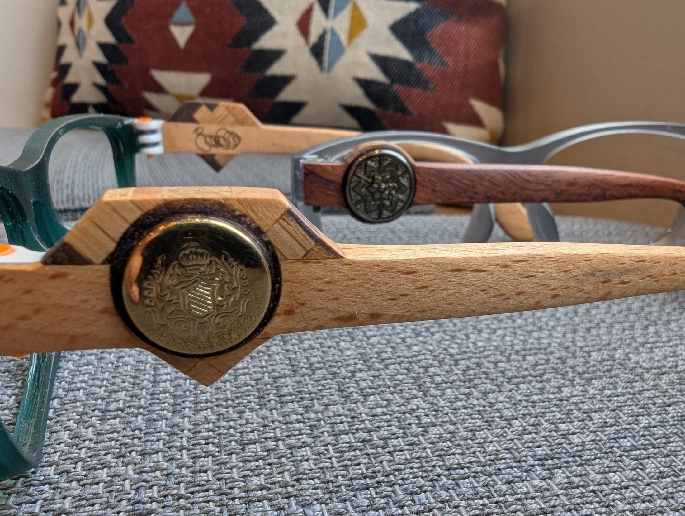 Two pairs of handmade eyeglasses with wood temples and brass medallions, one in pale maple and one in dark mahogany, displayed side by side