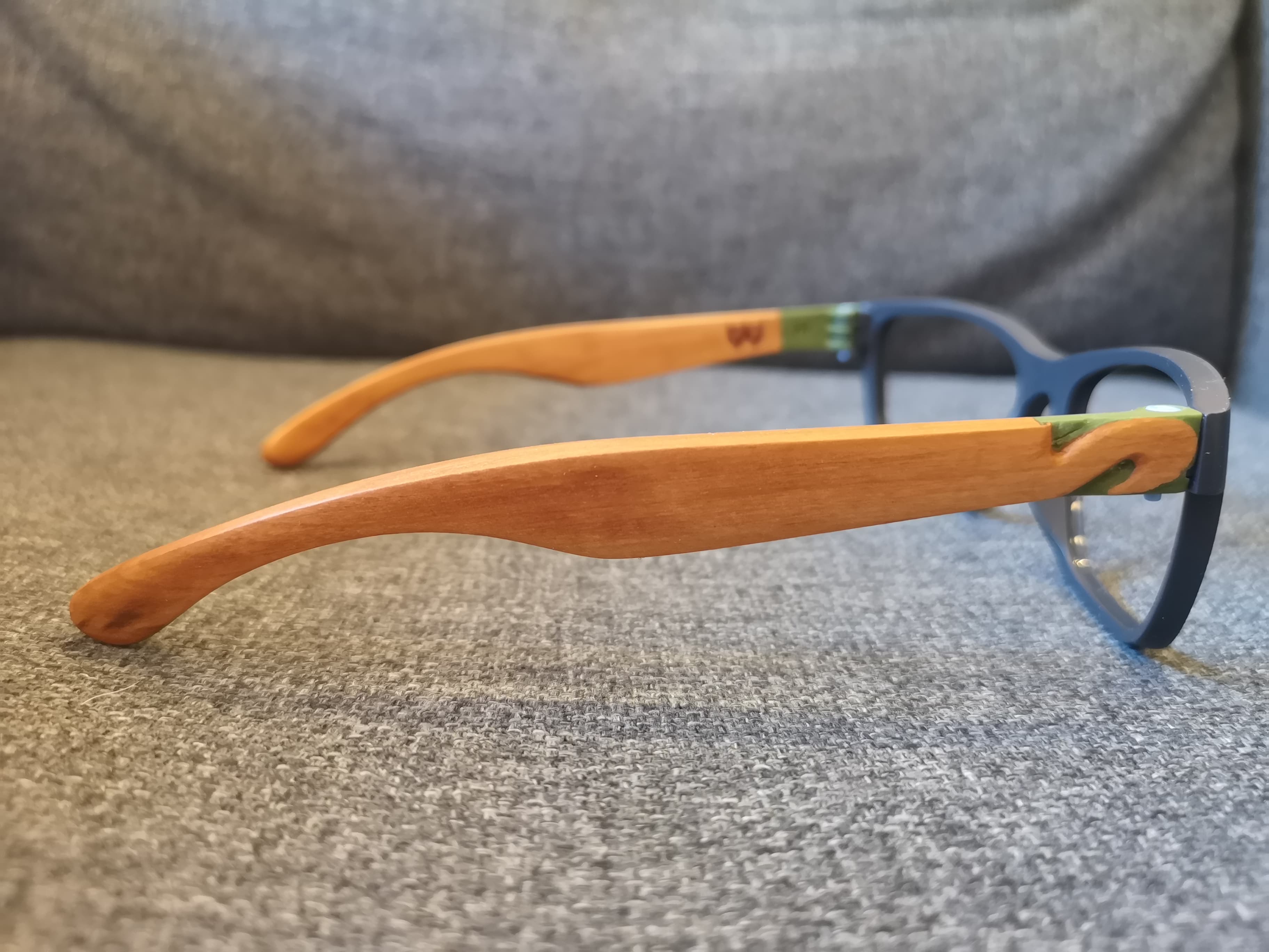 Side profile of navy eyeglasses with pale wood temples and a green resin hinge accent