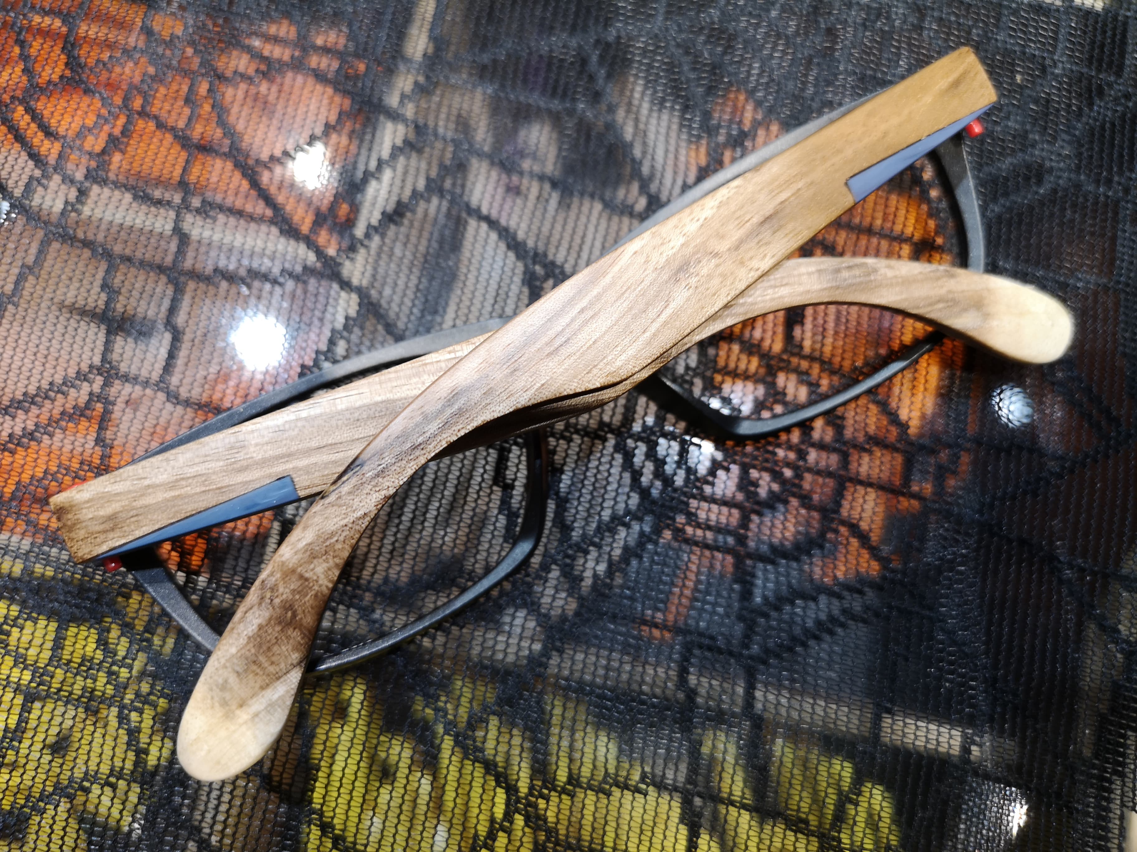 Black eyeglasses with pale driftwood-toned wood temples resting on fabric