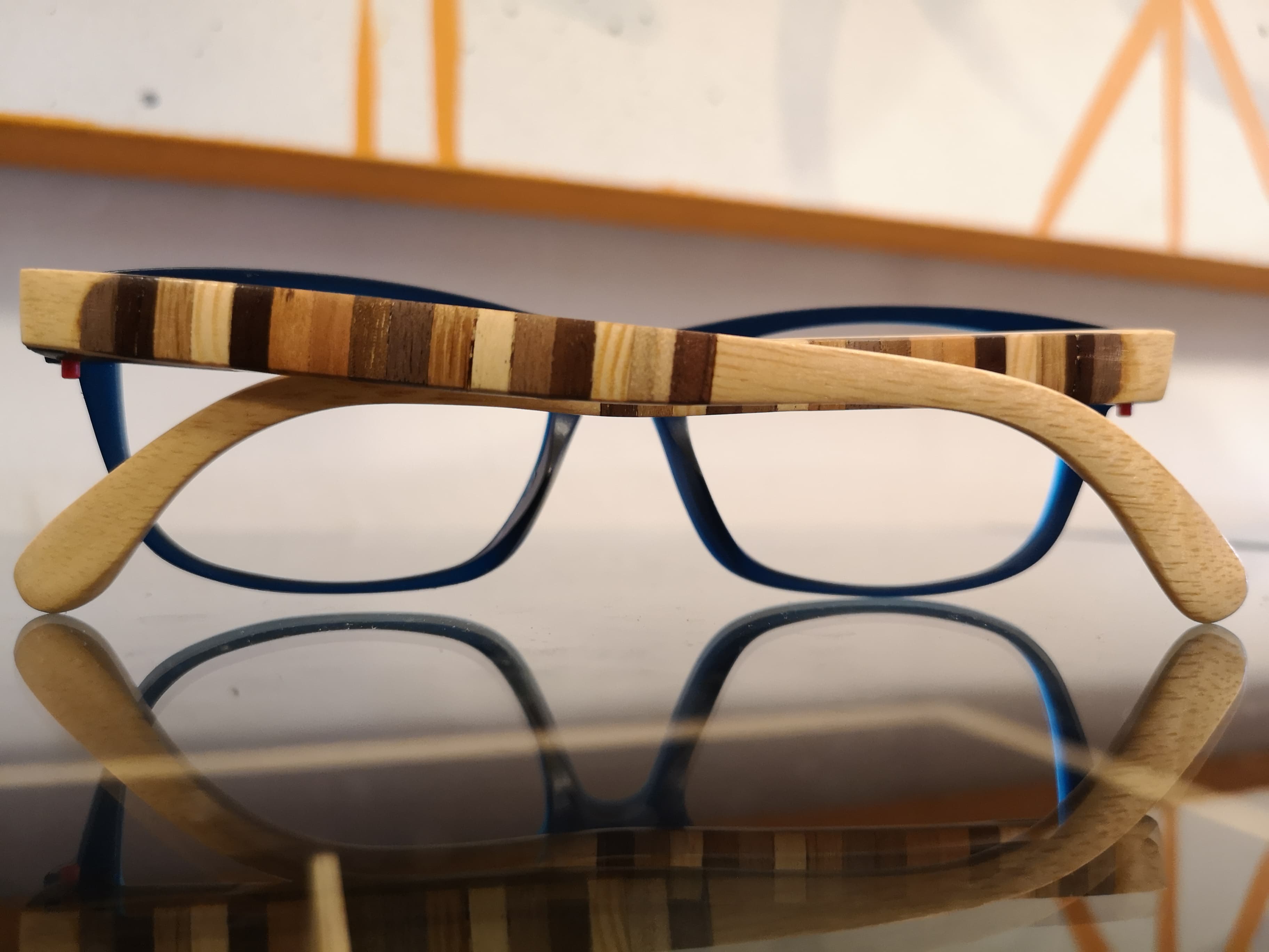 Royal blue eyeglasses with pale maple temples and a decorative multi-wood stripe inlay, resting on a reflective surface