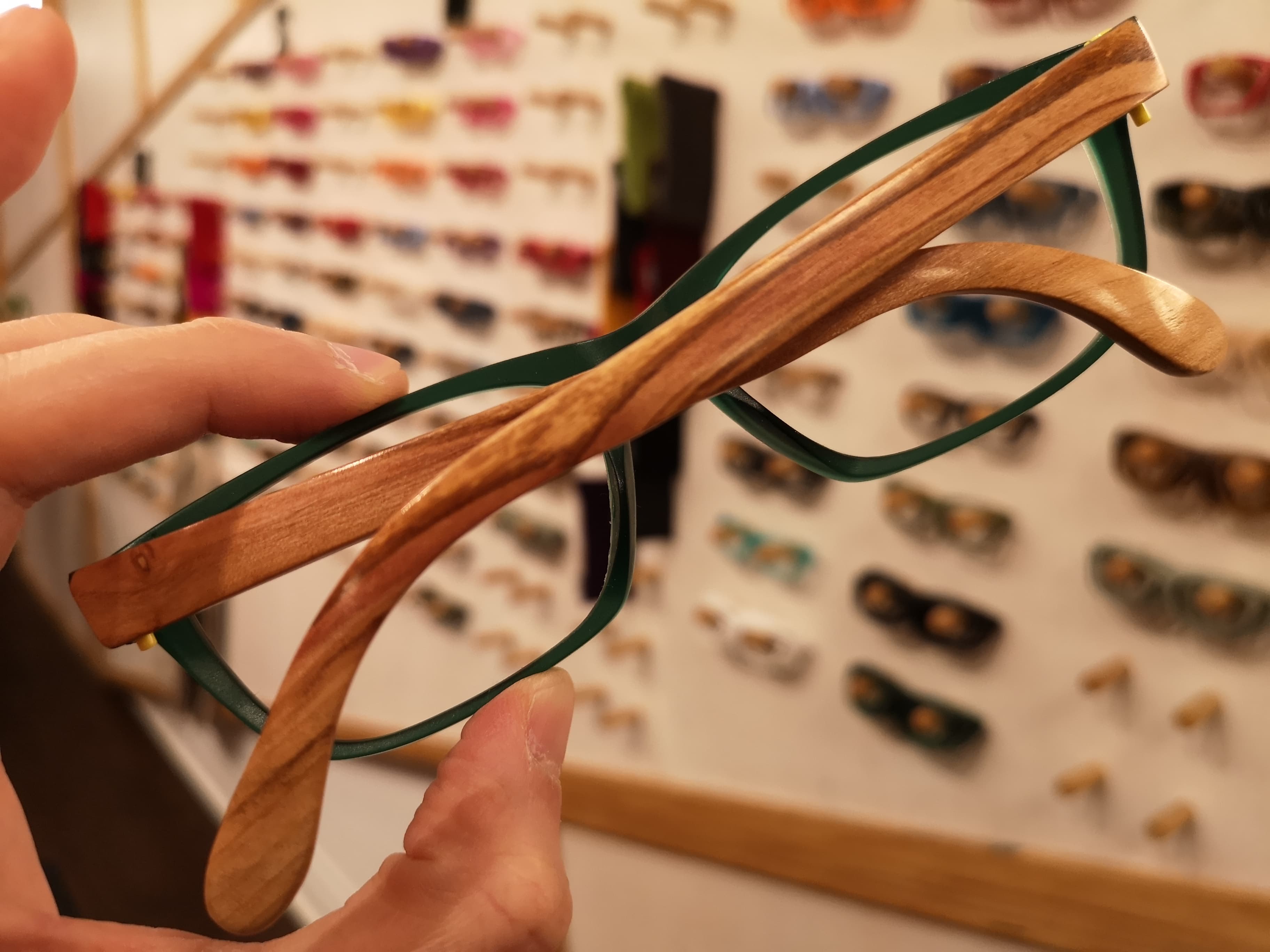 Forest green eyeglasses with plain olive wood temples displayed in an optical setting