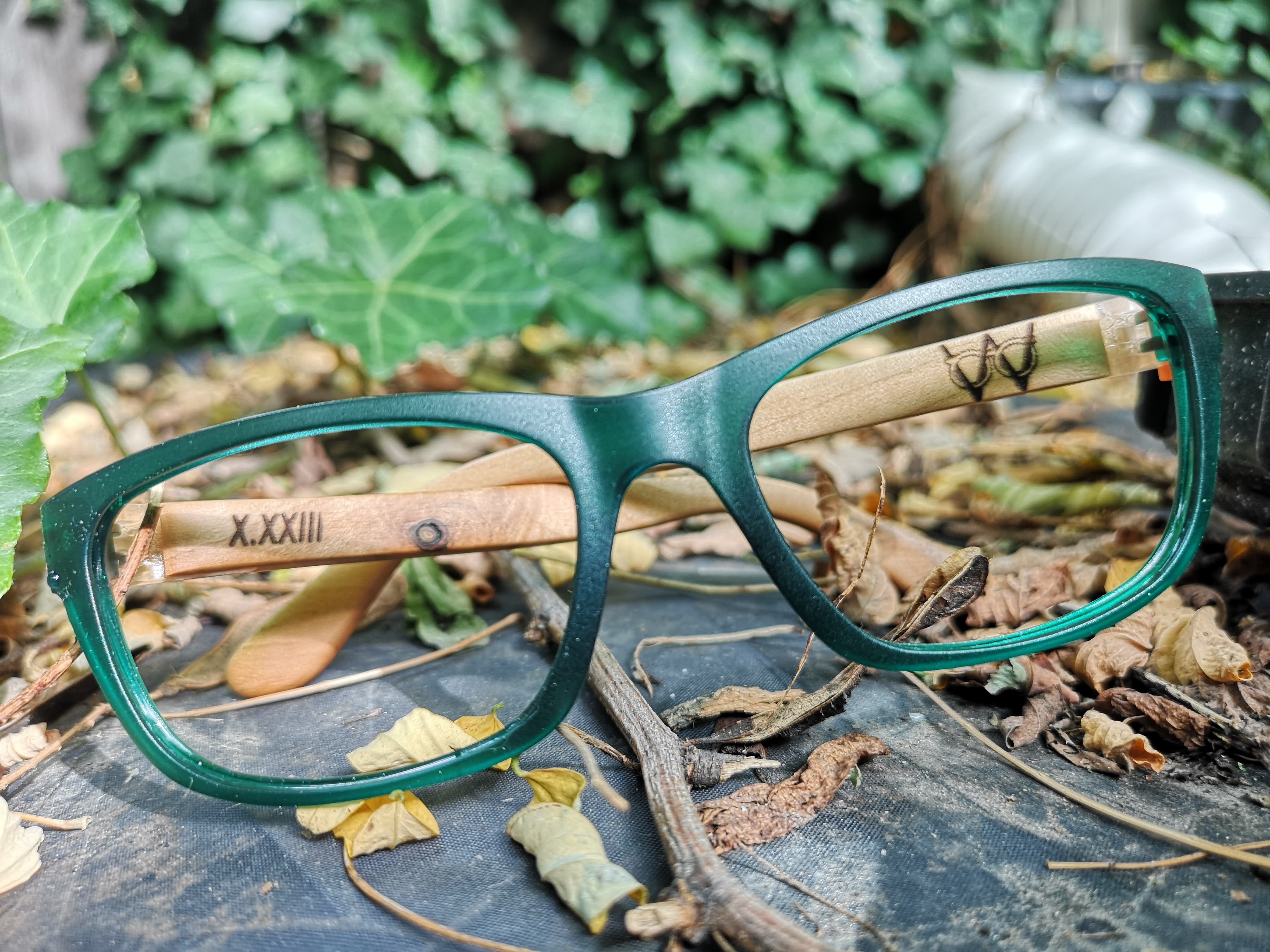 Dark teal eyeglasses with maple temples engraved with a maker's mark, photographed outdoors