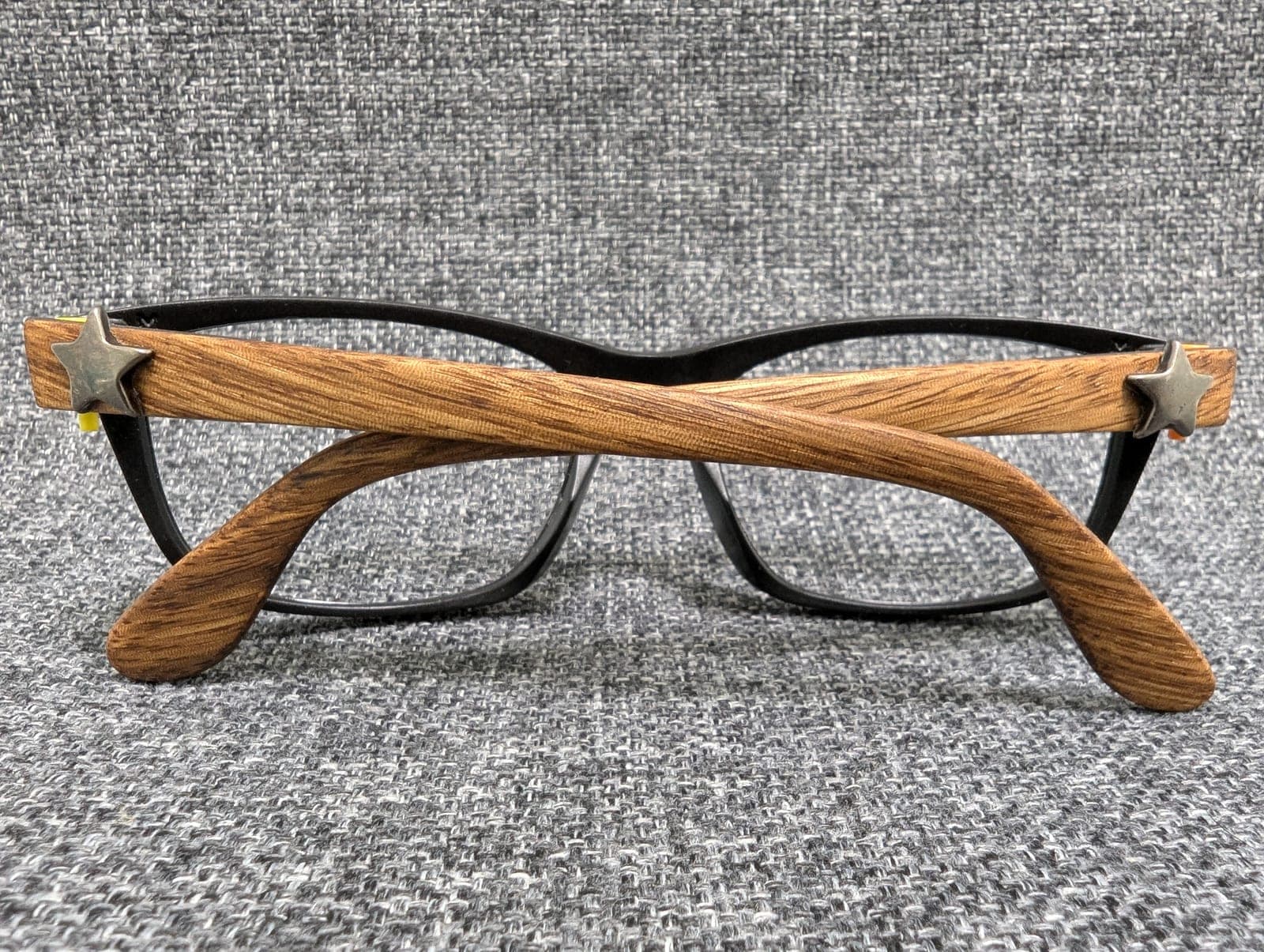 Black upcycled material eyeglass frames with golden oak wood temples, each set with a metal star stud