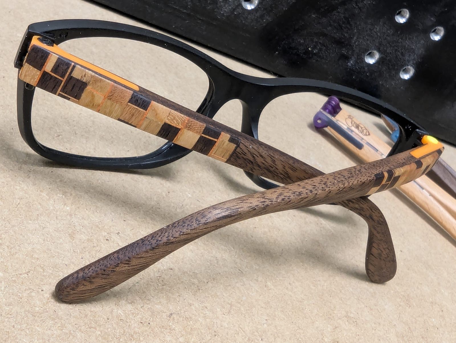 Black upcycled material eyeglasses with walnut wood temples featuring a rainbow chevron-striped inlay