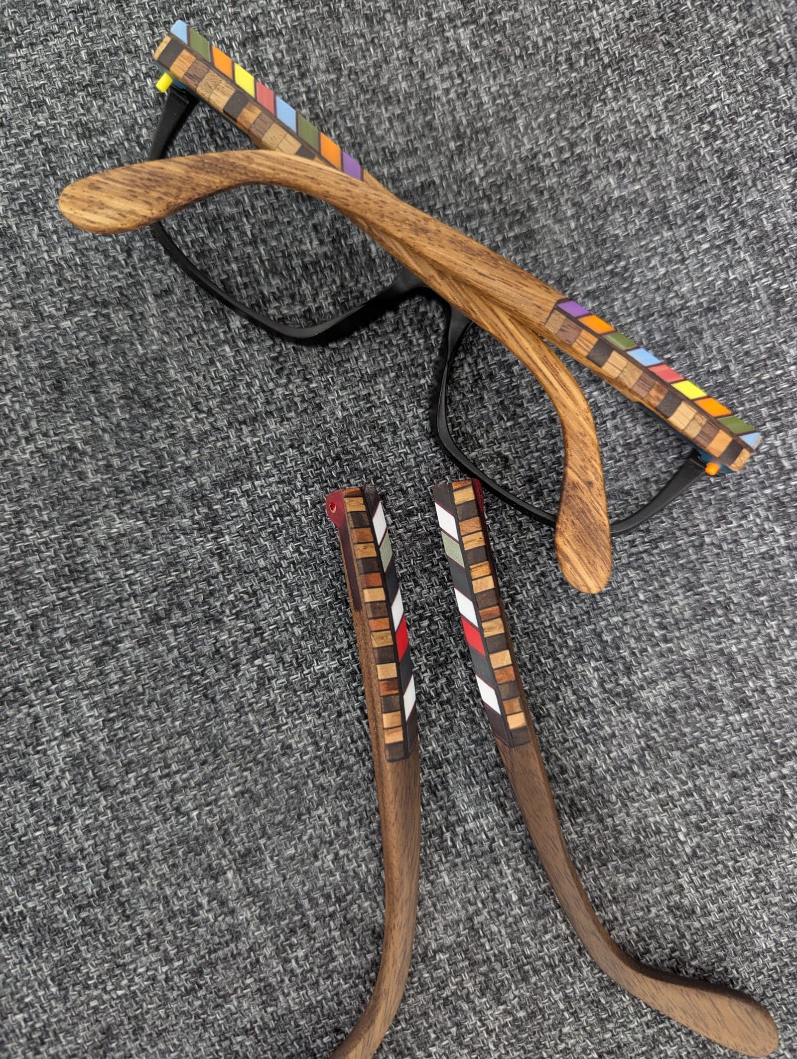 Top view of black upcycled material eyeglasses with walnut wood temples featuring a colorful checkerboard mosaic inlay