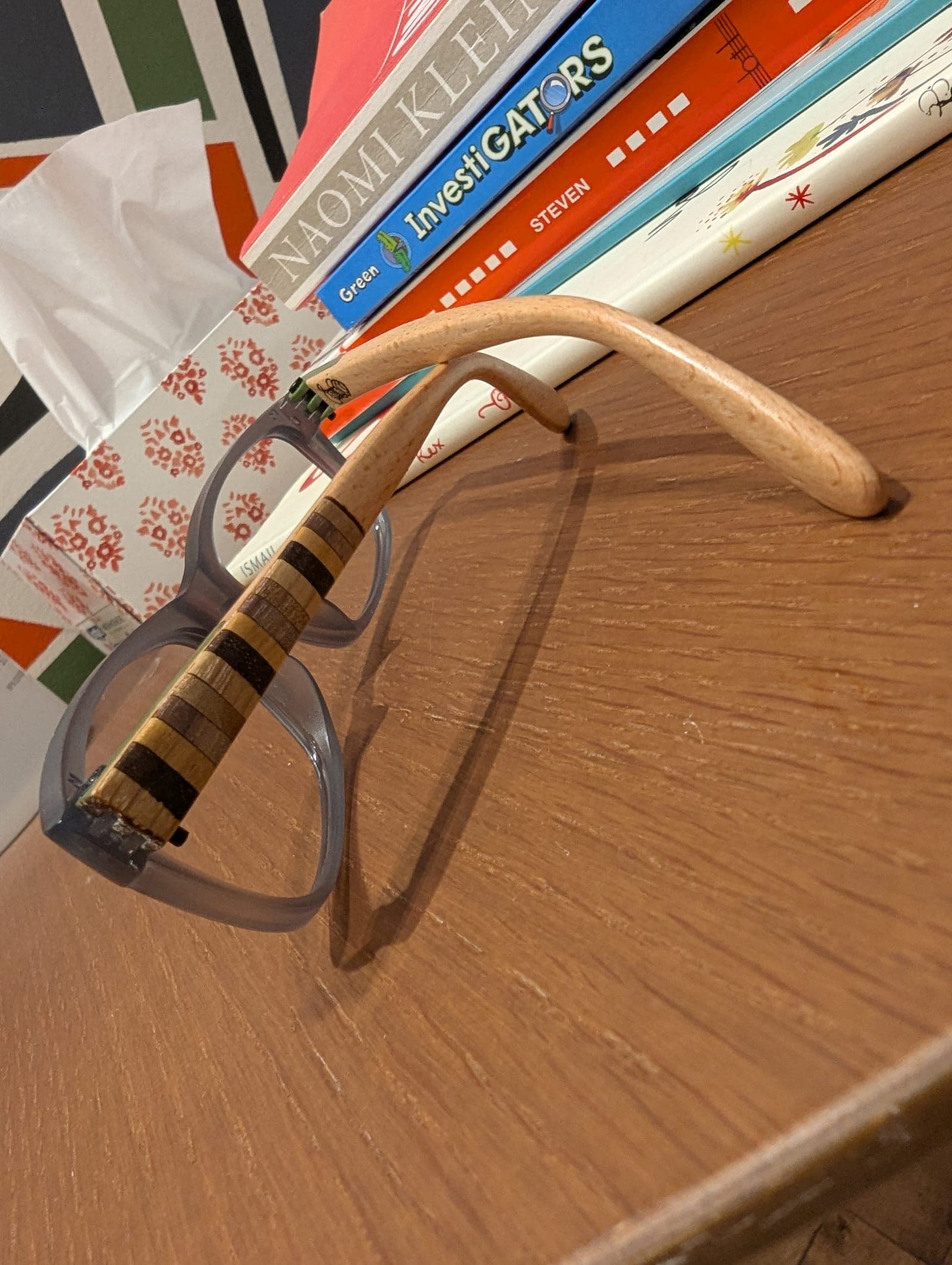 Burgundy upcycled material eyeglass frames with a rainbow-striped edge, paired with a light oak wood temple
