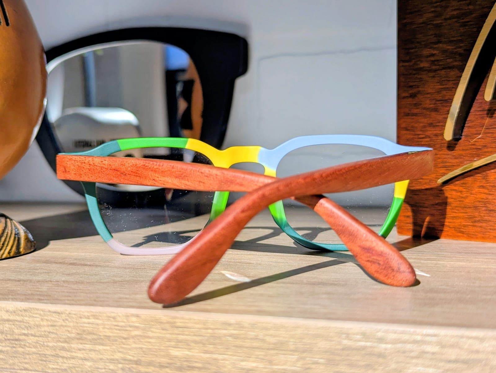 Color-block upcycled material eyeglasses with mahogany wood temples resting on a wood table in front of a houseplant
