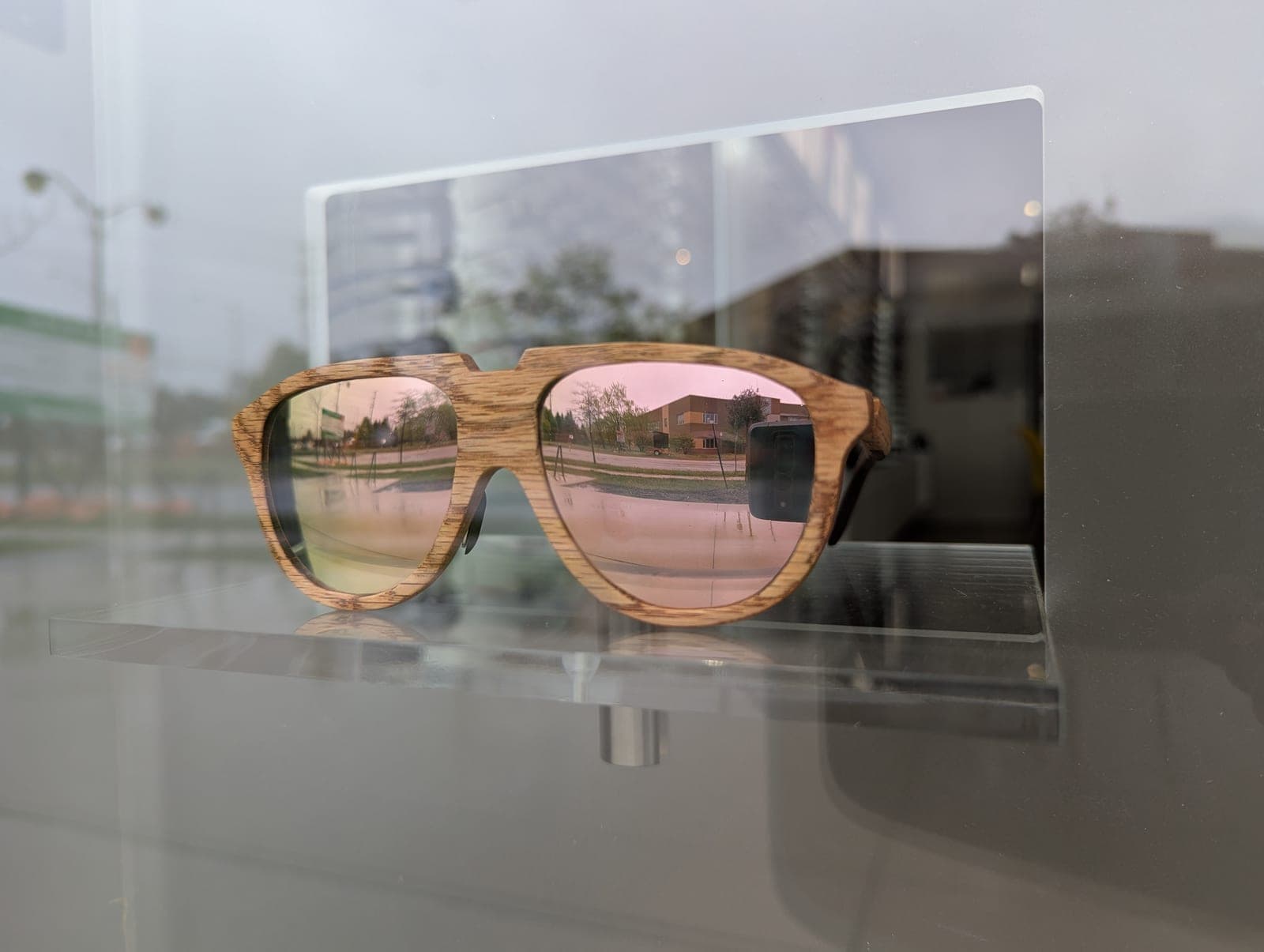 Golden oak wood aviator sunglasses with rose-pink mirrored lenses on a display stand