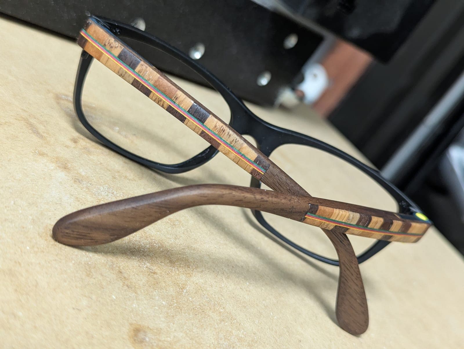 Smoke-tinted upcycled material eyeglass frames with deep reddish rosewood temples and a small engraved geometric medallion