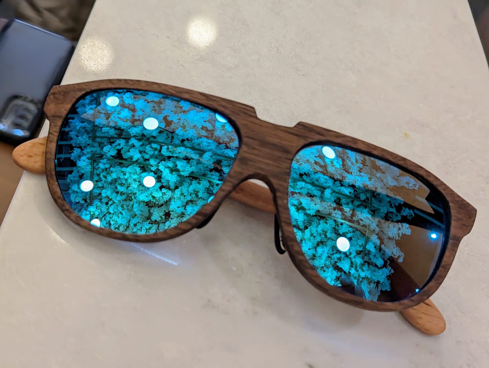 Wood-framed aviator sunglasses with blue mirrored lenses and beech temples resting on a wooden table