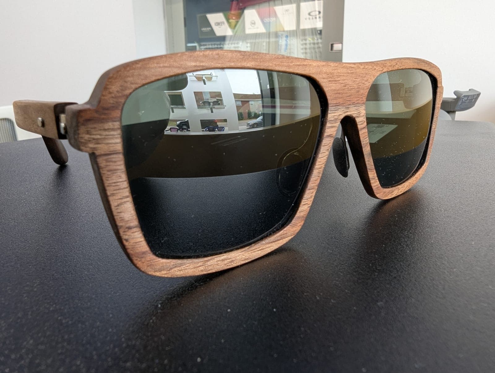 Walnut wood sunglasses with square frames and green-gold mirrored lenses, shown on a dark display surface