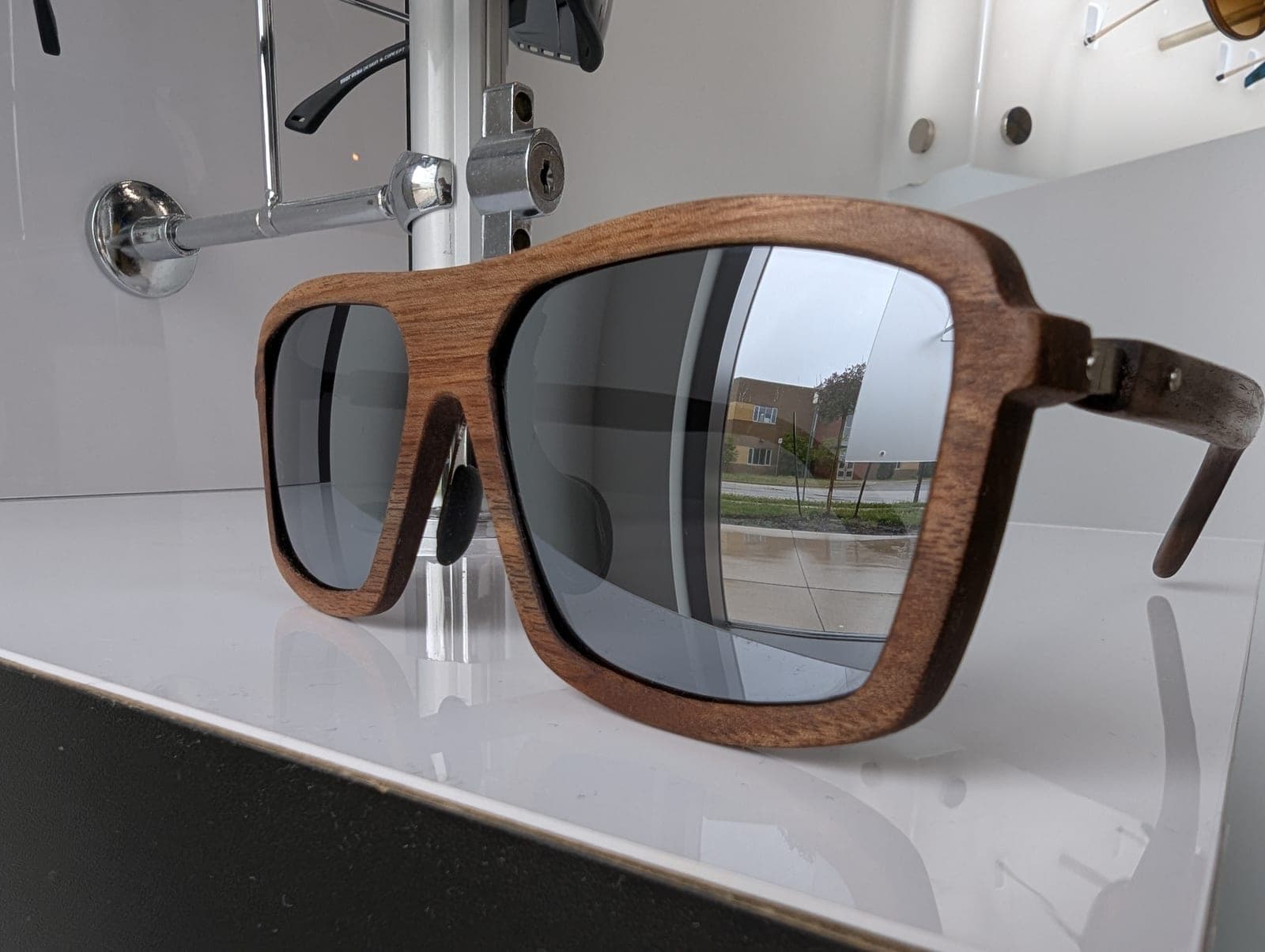 Walnut wood sunglasses with silver mirrored lenses displayed on a glass shelf
