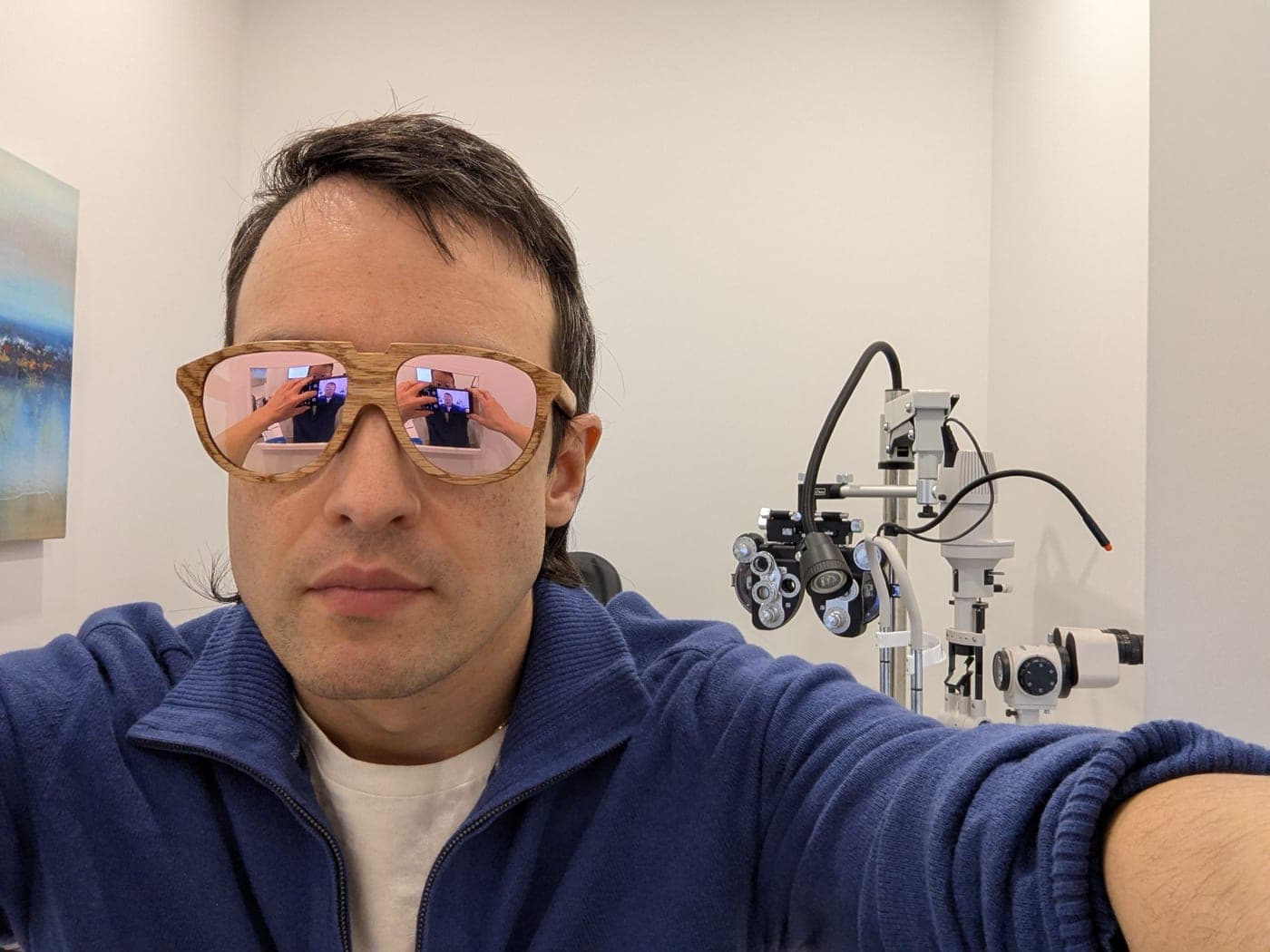The maker wearing a pair of wood-textured glasses while sitting in an eye exam chair