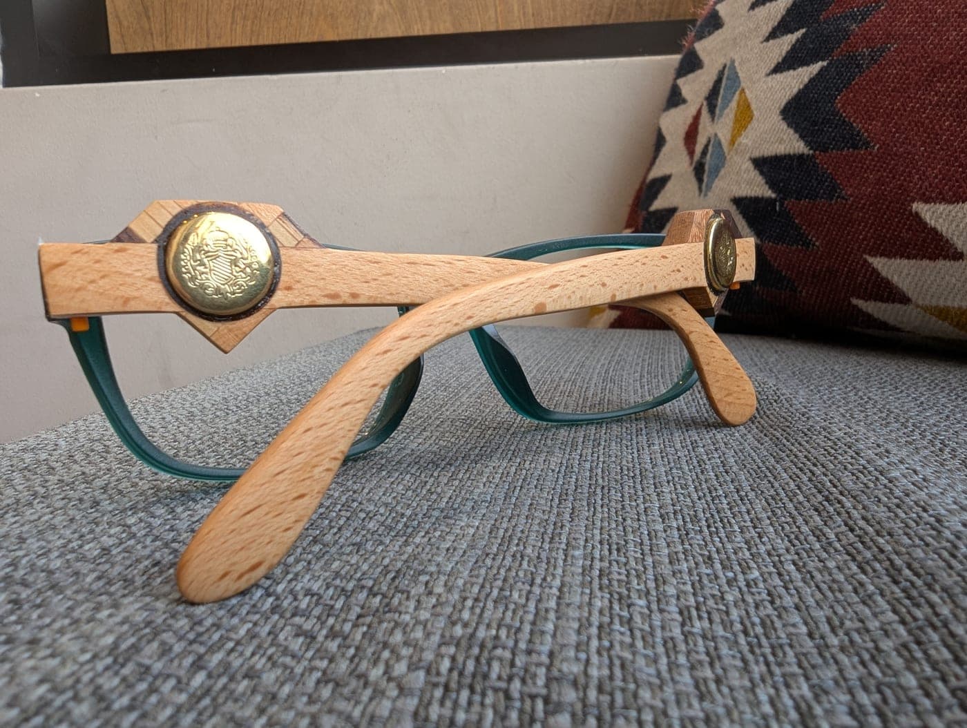 Close-up of light maple wood temples with a brass medallion resting against a woven southwestern-patterned pillow
