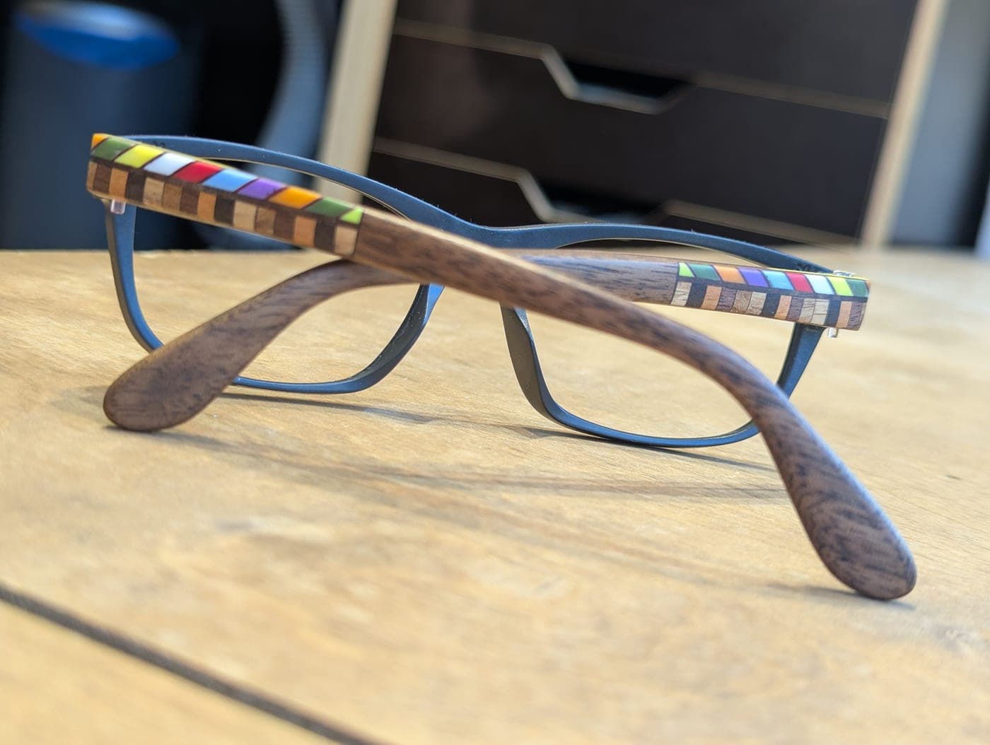 Finished eyeglasses with walnut wood temples and checkerboard mosaic inlay, shown on a workbench