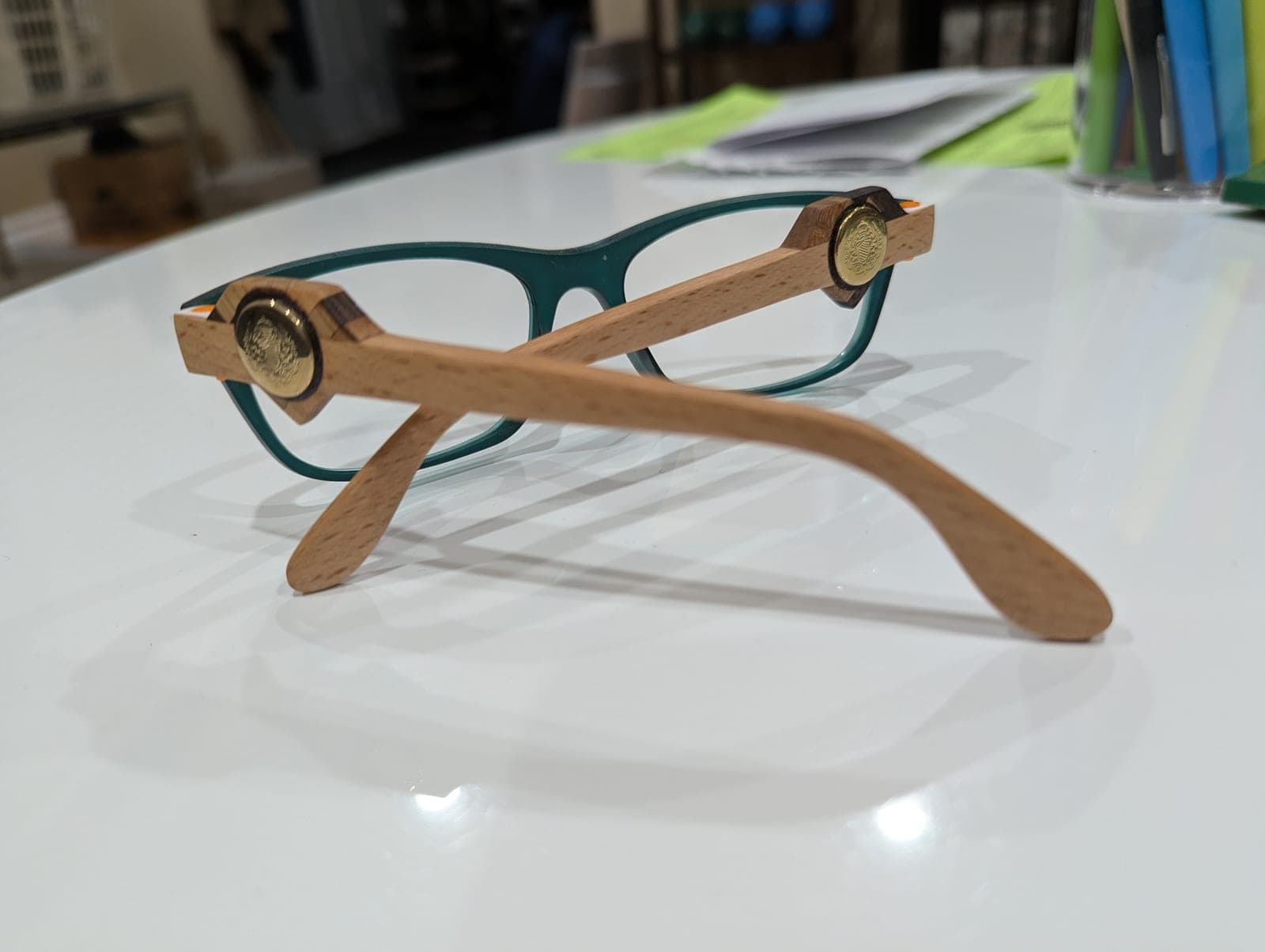Black upcycled material eyeglass frames with dark walnut wood temples, each inlaid with a carved ivory-colored skull medallion, viewed from behind