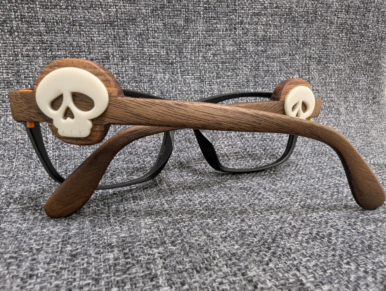 Close-up of a dark walnut wood temple with a carved skull medallion inlay on black upcycled material frames