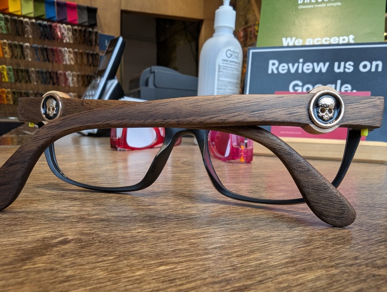 Walnut wood temples with carved skull medallions on black upcycled material frames, displayed in an optical shop