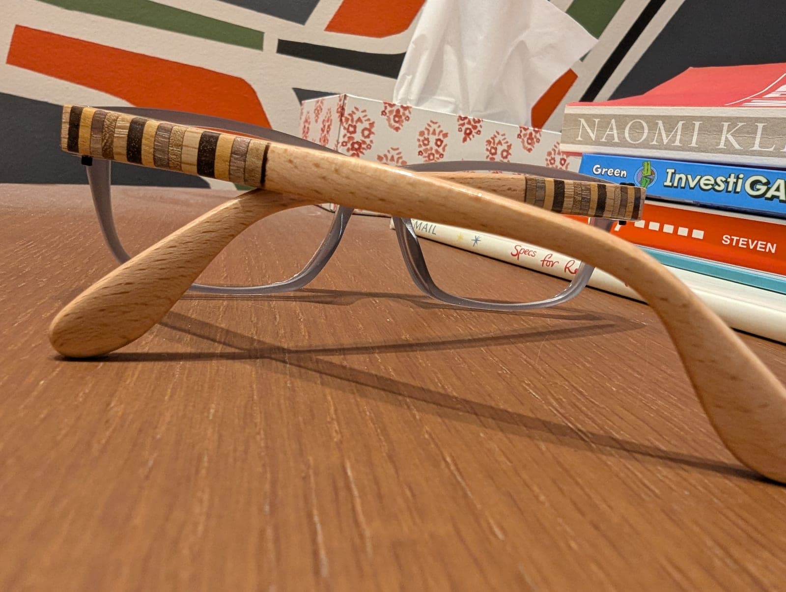 Close-up of burgundy upcycled material frames with rainbow stripe detailing and an oak wood temple