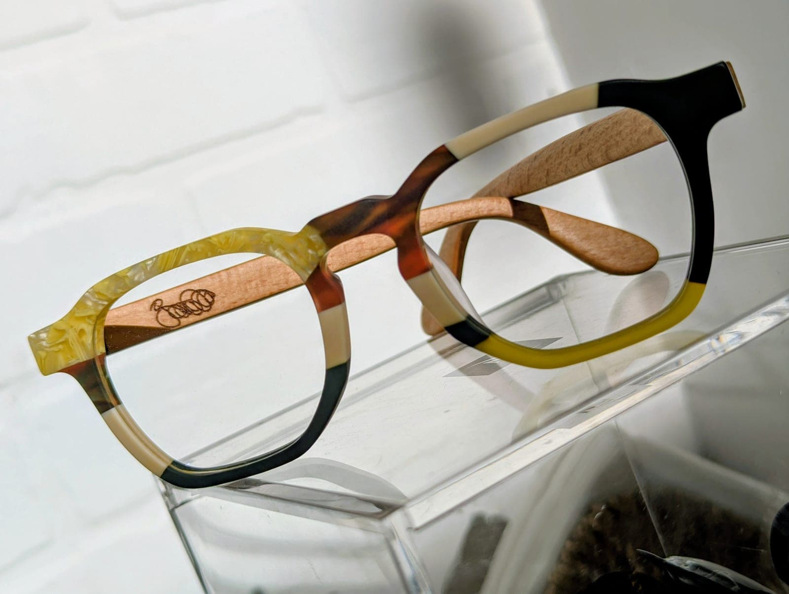 Angled view of tortoiseshell upcycled material frames with maple wood temples and an engraved maker's mark